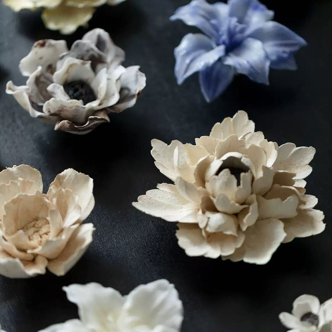 Ceramic flowers with sculpted petals arranged on a dark surface