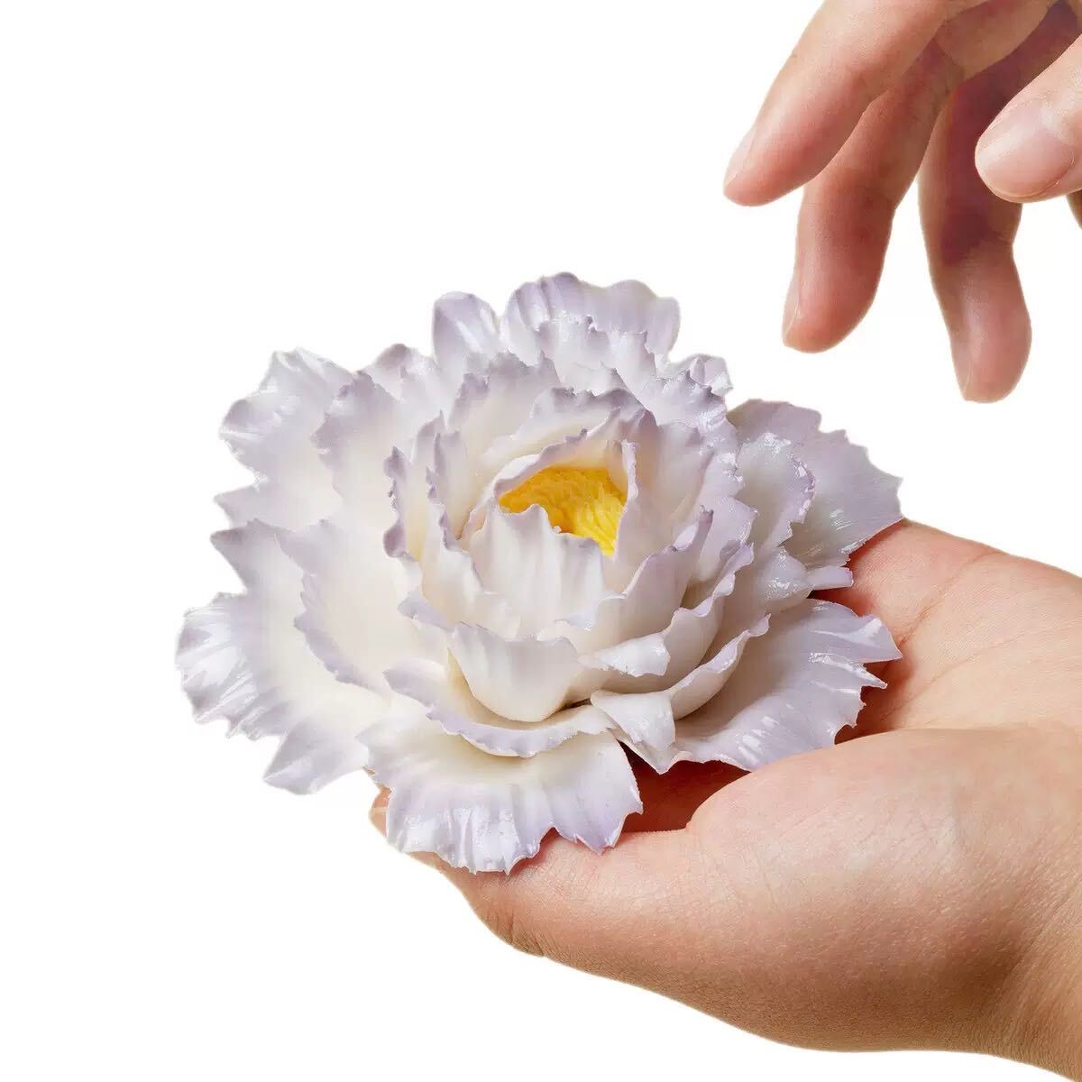 Hand holding a white ceramic flower with a yellow center against a white background